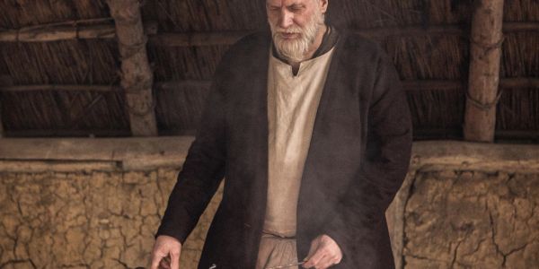Bearded man in medieval attire cooking outdoors.