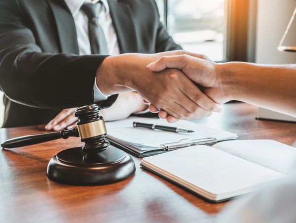 Two people shaking hands over a legal desk with a gavel and documents.