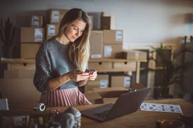 Working woman at online shop. She wearing casual clothing and using laptop and mobile phone for work organization