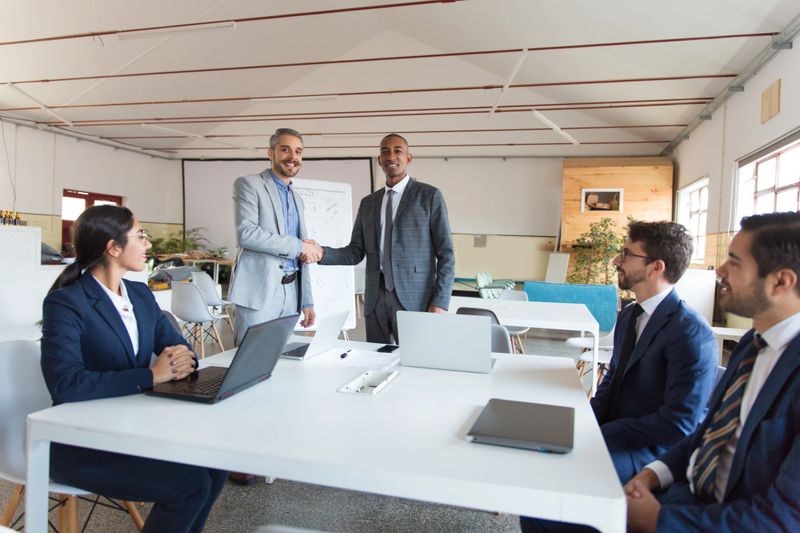 Two businessmen shaking hands in office. Smiling colleagues standing and looking at camera. Business meeting concept