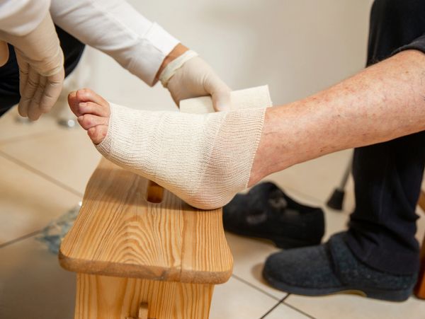 A person's ankle is being wrapped with a bandage by a gloved hand.