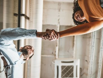Two people smiling and shaking hands in a modern office.