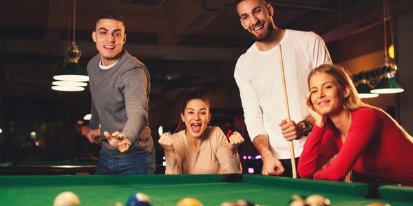 Four friends enjoying a lively game of pool at night.