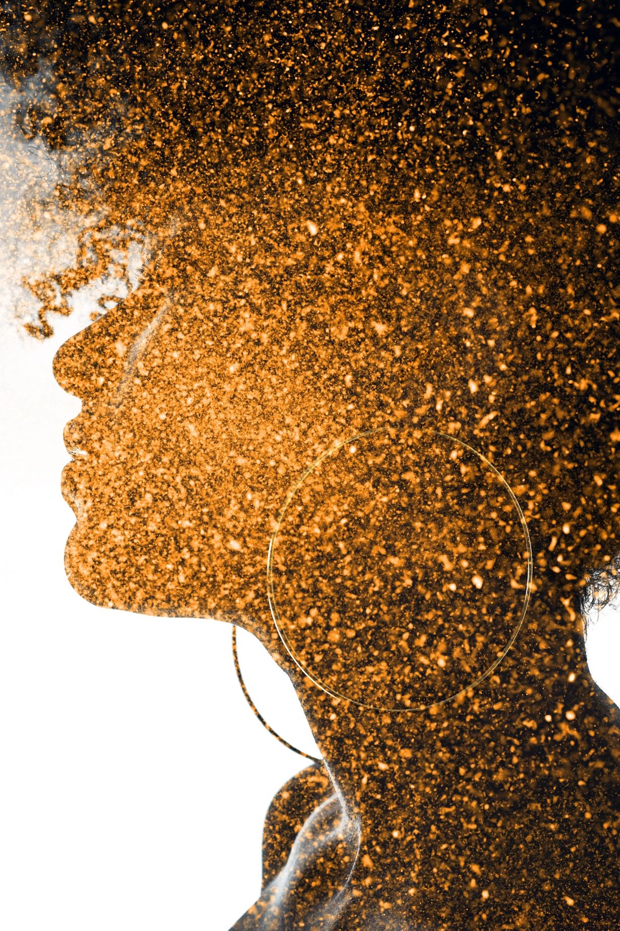 Profile of a woman with curly hair and large hoop earrings covered in golden glitter.