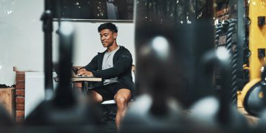 A man sitting and smiling at a laptop in a gym.
