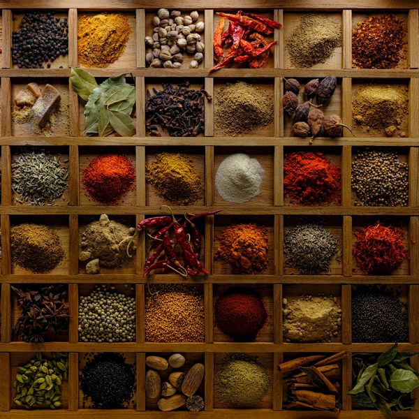 A wooden box with assorted colorful spices and herbs arranged in compartments.