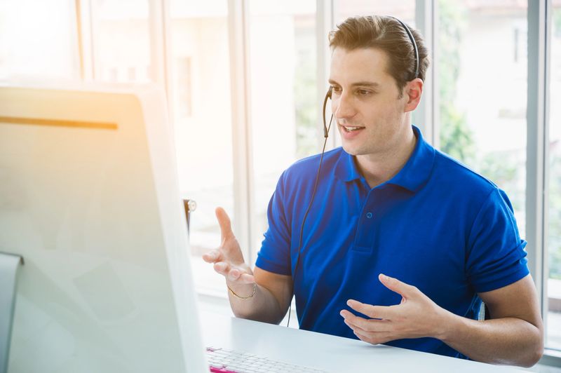 Male customer support operator at work. Team Business and Delivery call center in office. Working with a headset in blue uniform.