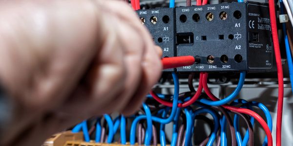 Close-up of hand wiring electrical control panel with red and blue cables.