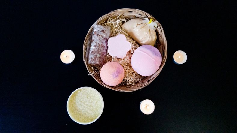A set of beauty items. Bath salt, bath bombs, and milk powder in a basket. Romantic atmosphere-candles are lit. Black table. Body care, rest after a hard day.