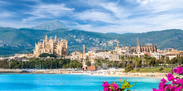 Scenic view of a coastal city with a cathedral and mountains.
