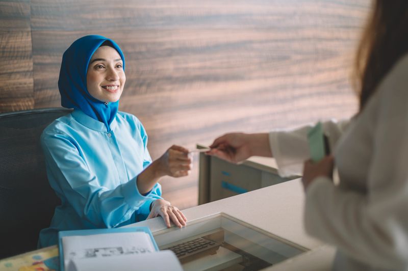 malaysia hospital registration counter asian female receptionist getting payment from the female hijab Muslim patient accepting her credit card