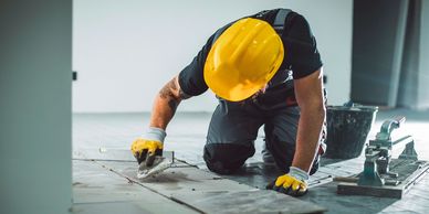 Construction worker tiling floor while wearing safety gear.