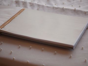 An open spiral-bound notebook with blank pages on a textured fabric surface.