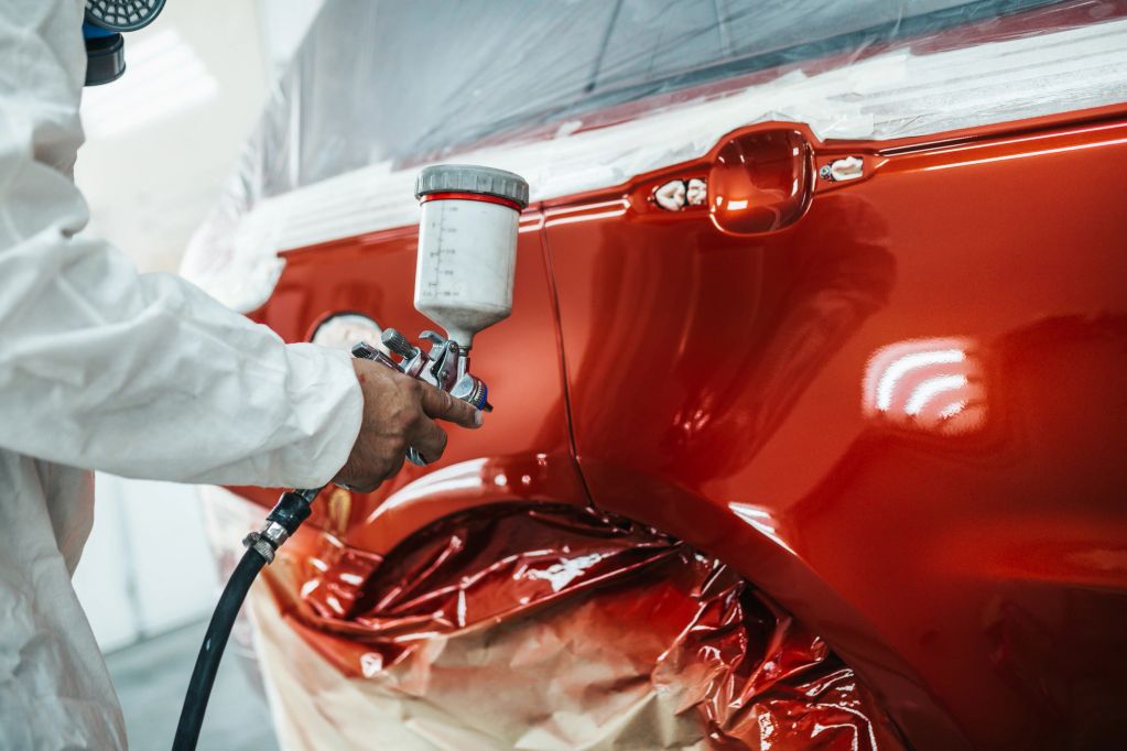 Person spray painting a red car door.