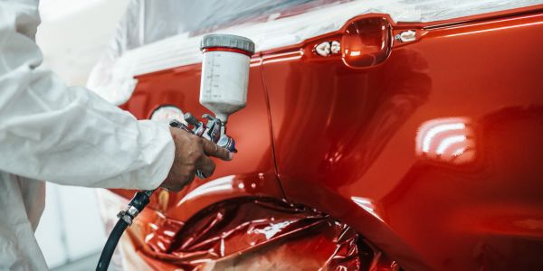 Person lackiert ein rotes Auto mit Spritzpistole.