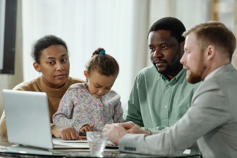 Adult black man with family listening to financial adviser giving presentation on laptop while consulting on home loan