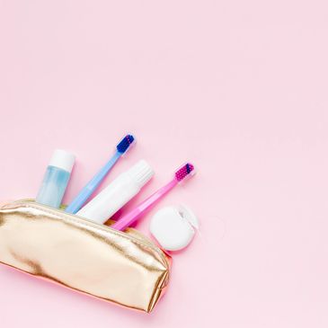 Gold toiletry bag with toothbrushes, toothpaste, mouthwash, and dental floss on pink background.