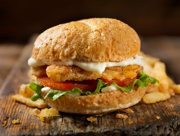 Crispy chicken sandwich with lettuce, tomato, and mayo on a rustic bun.
