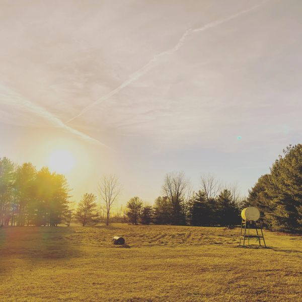 Sunset over an open field with trees and a water feeder.