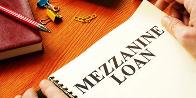Hands holding a notebook with 'MEZZANINE LOAN' text on a wooden desk.