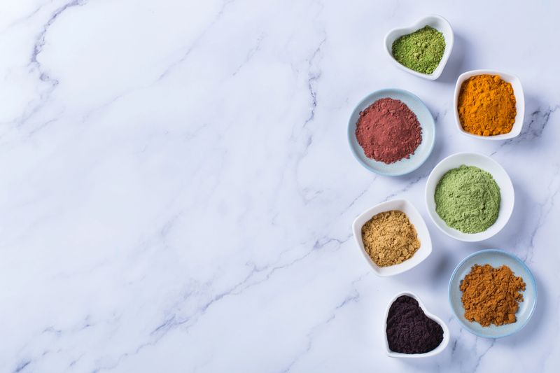 Balanced nutrition concept for clean eating antioxidant detox diet. Assortment of superfood powder - acai, turmeric, wheat, ginger, cinnamon, matcha. Flat lay, copy space marble background