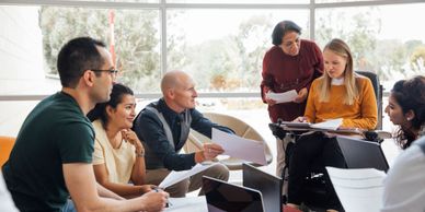 Group of diverse people collaborating with papers and laptops in a bright room.