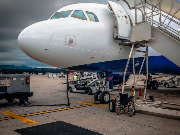 Airplane parked with open door and wheelchair nearby on a cloudy day.