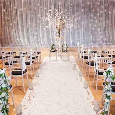 Elegant indoor wedding aisle with white chairs and fairy lights.