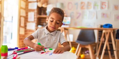 Young boy drawing with markers at a table.