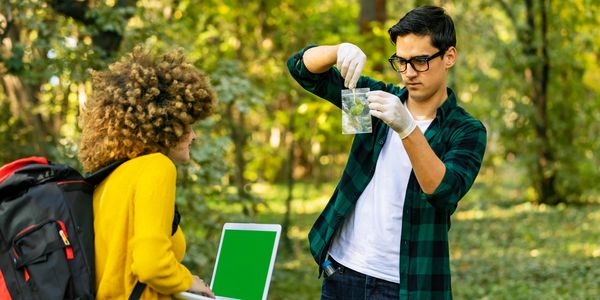 Two students examining a water sample outdoors in a forest.