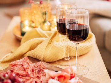 Two glasses of red wine with charcuterie on a wooden table.