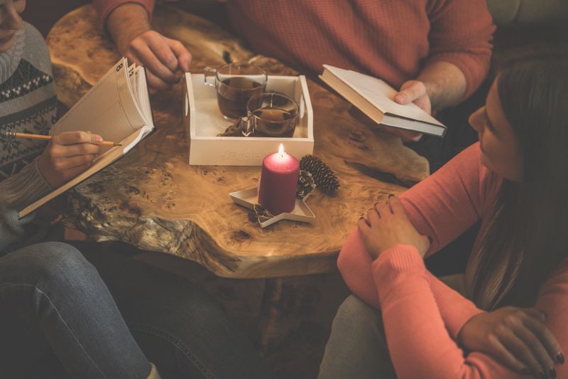 High angle view of small group of friends sitting on the floor around the coffee table, hanging out, chatting and playing games while enjoying warm tea together.