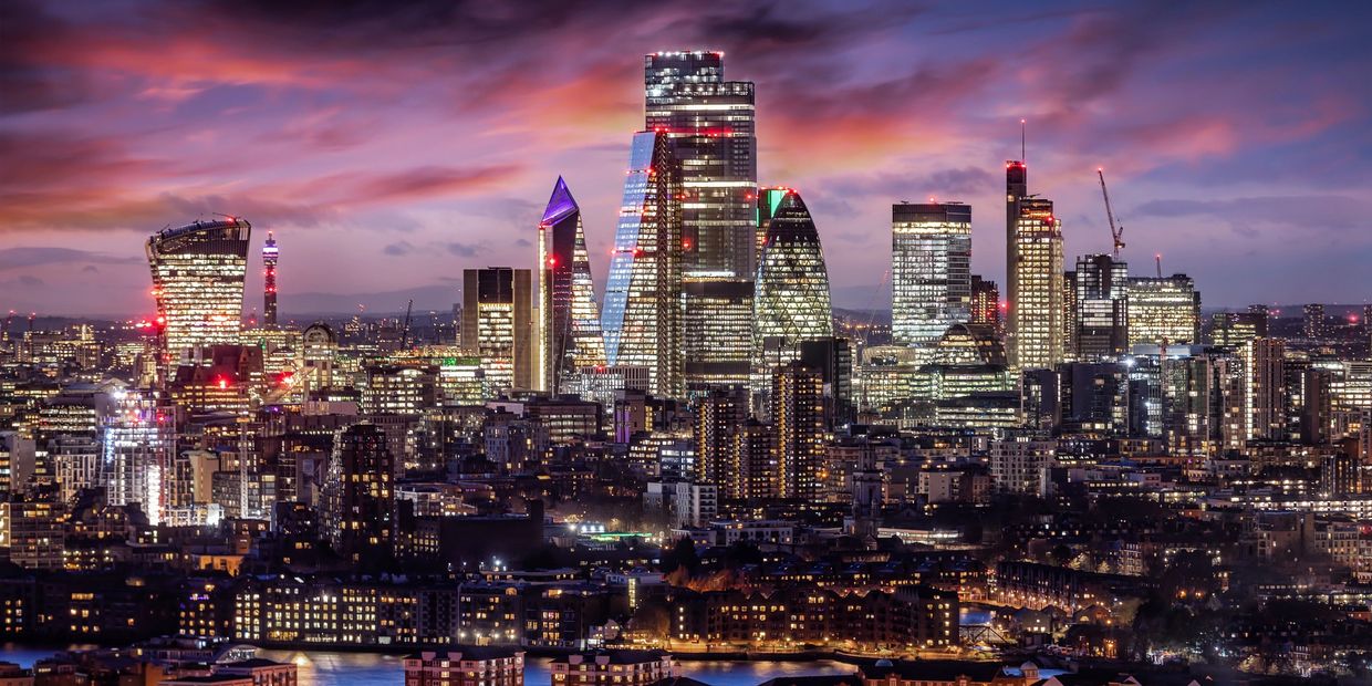 Nighttime cityscape of London with illuminated skyscrapers and a colorful sky.