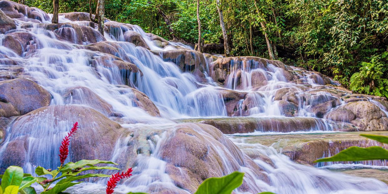 Multi-tiered waterfall flowing over smooth rocks surrounded by greenery.