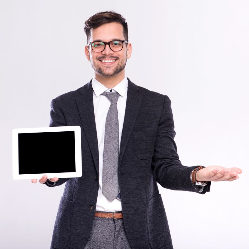 Young handsome male businessman standing in studio and looking at digital tablet computer