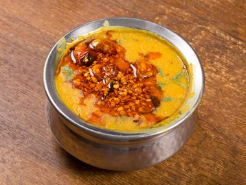 A bowl of yellow lentil dal garnished with spices and herbs.