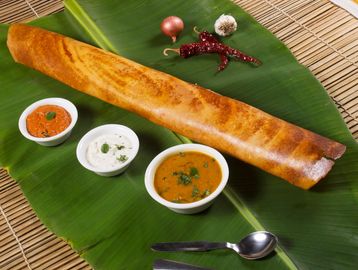 A crispy dosa served on a banana leaf with three different chutneys and garnishes.