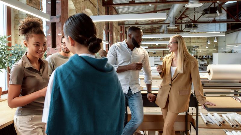 Portrait of mixed race business team having coffeebreak in office. Five colleagues in casual wear are talking and smiling while standing in co-working space. Team building concept. Horizontal shot