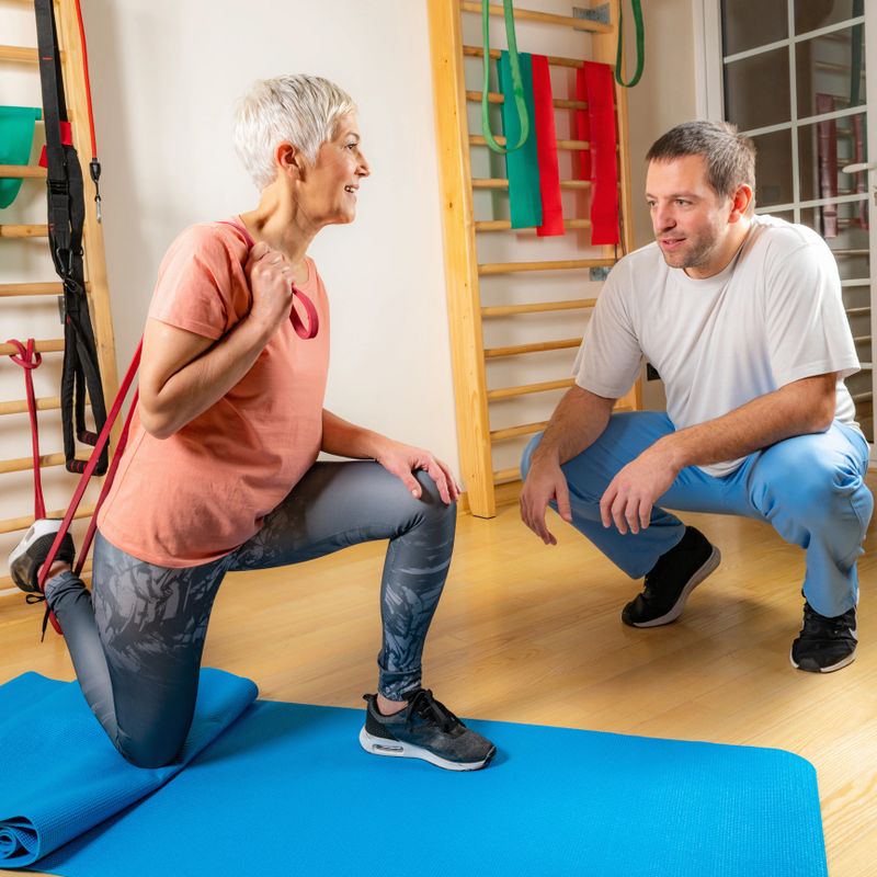 Senior woman exercising with rubber band in the gym with coach’s help