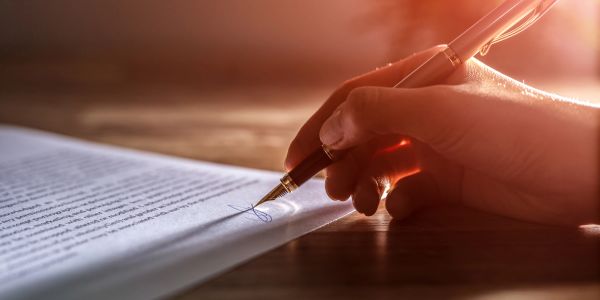 Hand signing a document with a pen.