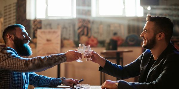 Two men smiling and toasting with drinks in a cozy bar.