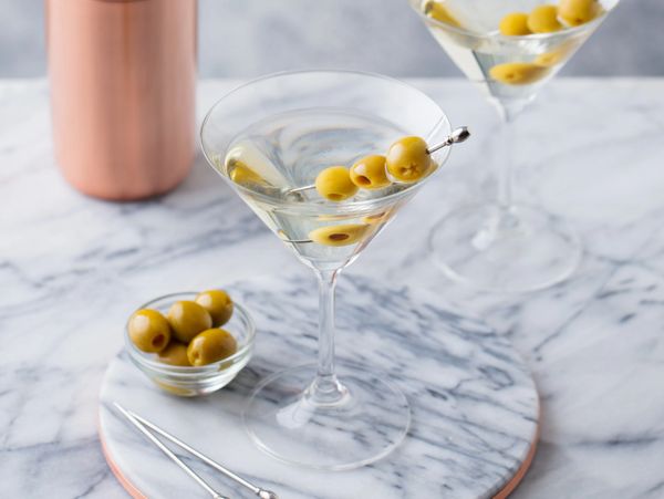 Two martini glasses garnished with green olives on a marble surface.