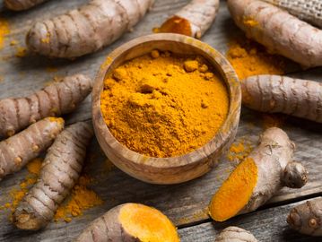 Turmeric powder in a wooden bowl surrounded by fresh turmeric roots.