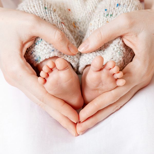 Adult hands forming a heart shape around a baby's feet.