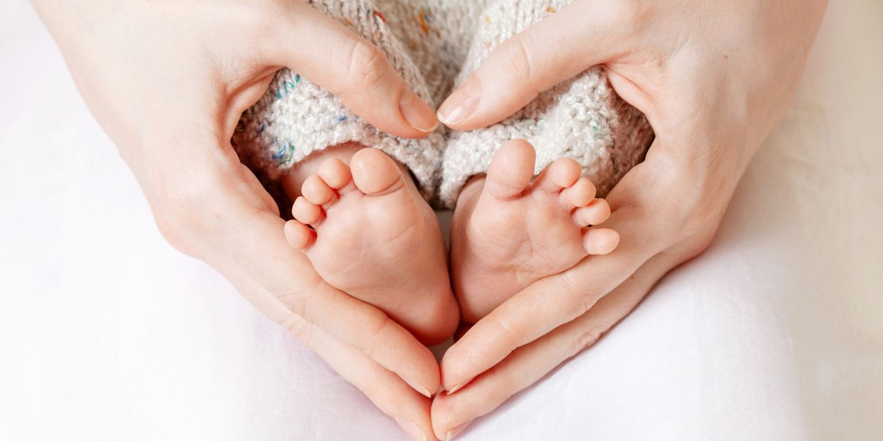 Adult hands forming a heart shape around baby feet.