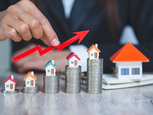 Hand pointing to rising arrow over houses.