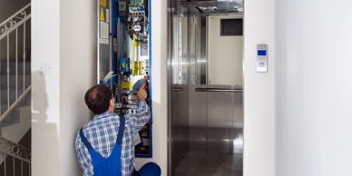 Technician repairs elevator control panel next to open elevator door.
