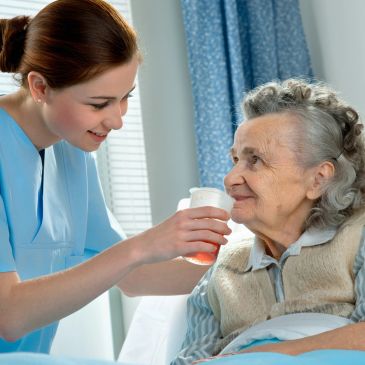 A nurse helps an elderly woman with medication, showing care and kindness.