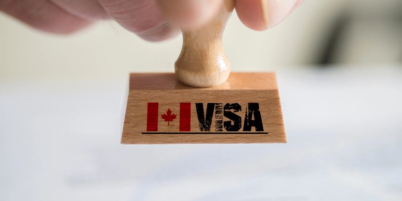 A hand holding a stamp with a Canadian visa logo.