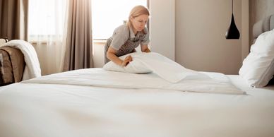 A woman making a bed with bright sunlight in the background.
